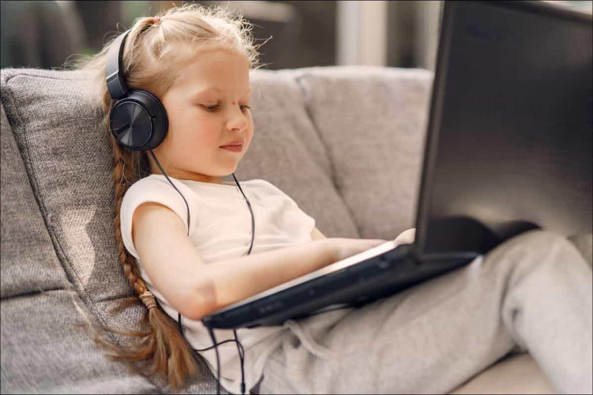 child using headphone and laptop sitting on sofa